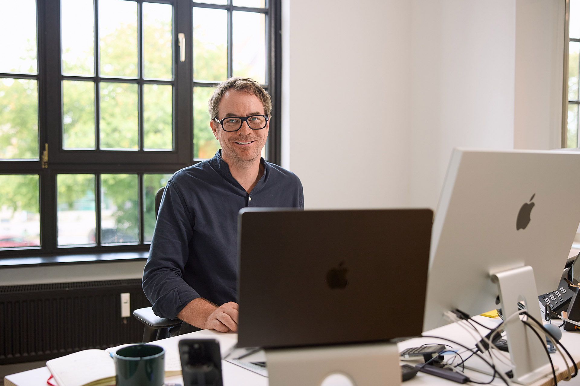 Kommunity Mitarbeiter am Schreibtisch, mit einem aufgeräumten und gut organisierten Arbeitsplatz. Diese Detailaufnahme von Karsten Koch zeigt das technische Know-how und die moderne Arbeitsweise des Teams.