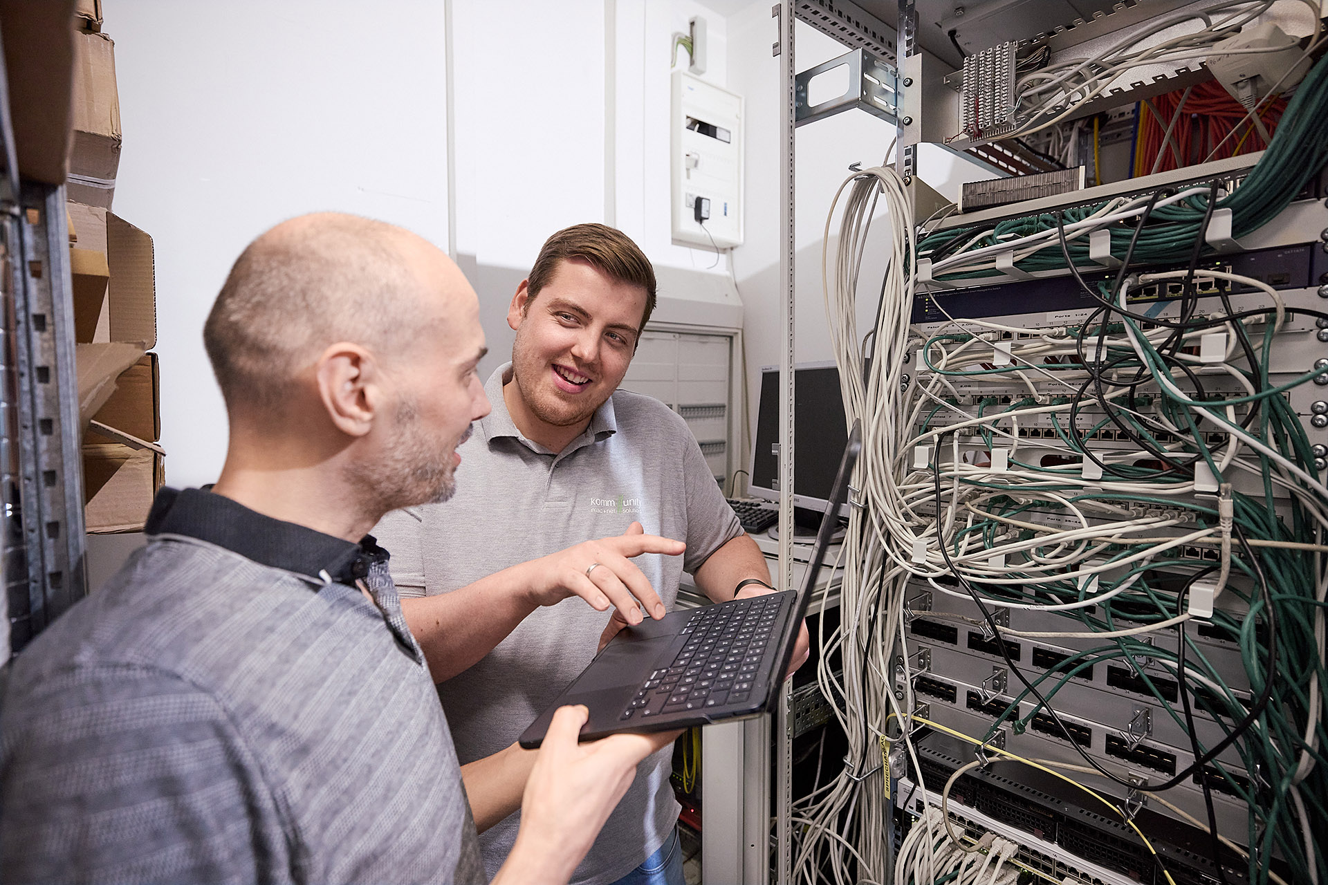 Zwei IT-Spezialisten von Kommunity Hannover im Serverraum bei einer Wartung, umgeben von Serverkabeln und Netzwerkgeräten. Professionelle Unternehmensfotografie von Karsten Koch für die visuelle Darstellung technischer Expertise im Bereich IT-Infrastruktur.